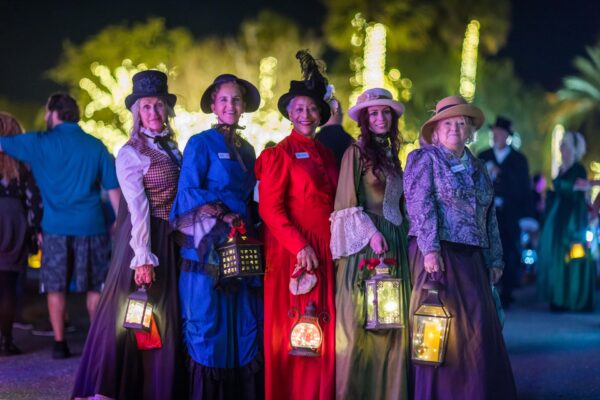 Women in Victorian costumes hold glowing lanterns during the illuminated procession at Dickens on Centre on Amelia Island