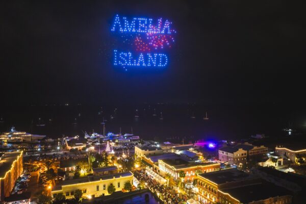 Drone show spells out Amelia Island in colorful lights above the illuminated Dickens on Centre festival at night