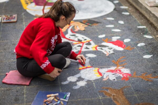 Artist in a red sweater draws holiday chalk art of reindeer and snowmen during Dickens on Centre on Amelia Island