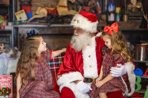 Santa Claus talks with two young girls in matching plaid dresses during Dickens on Centre on Amelia Island