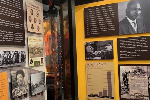 Museum exhibit featuring historical photos, documents, and text panels about African American business history, including portraits, a growth chart, and information on founders, milestones, and company achievements.