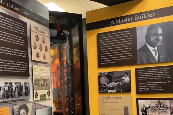 Museum exhibit displays panels about a Black business leader, including a portrait titled A Master Builder, historic photos, documents, and informational text about African American entrepreneurship and asset growth.
