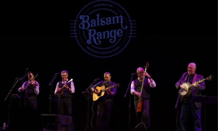 The bluegrass band Balsam Range performs on a stage beneath their logo.