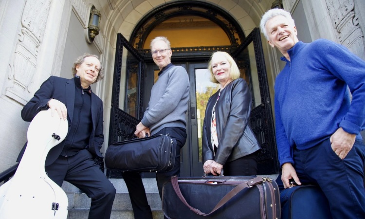 Four people stand in front of an arched building entrance, each holding a musical instrument case.