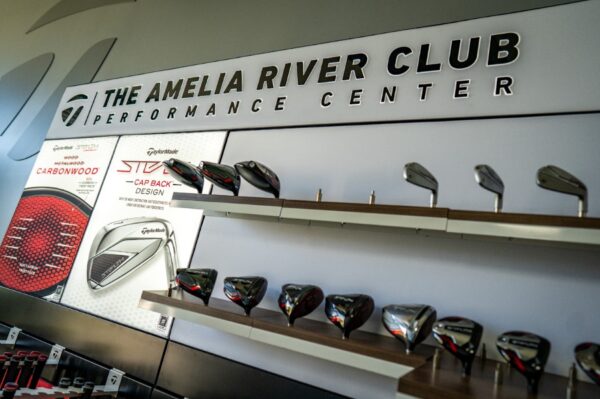 A display wall at The Amelia River Club Performance Center showcases various TaylorMade golf club heads and equipment, neatly arranged on shelves with branded signage above.