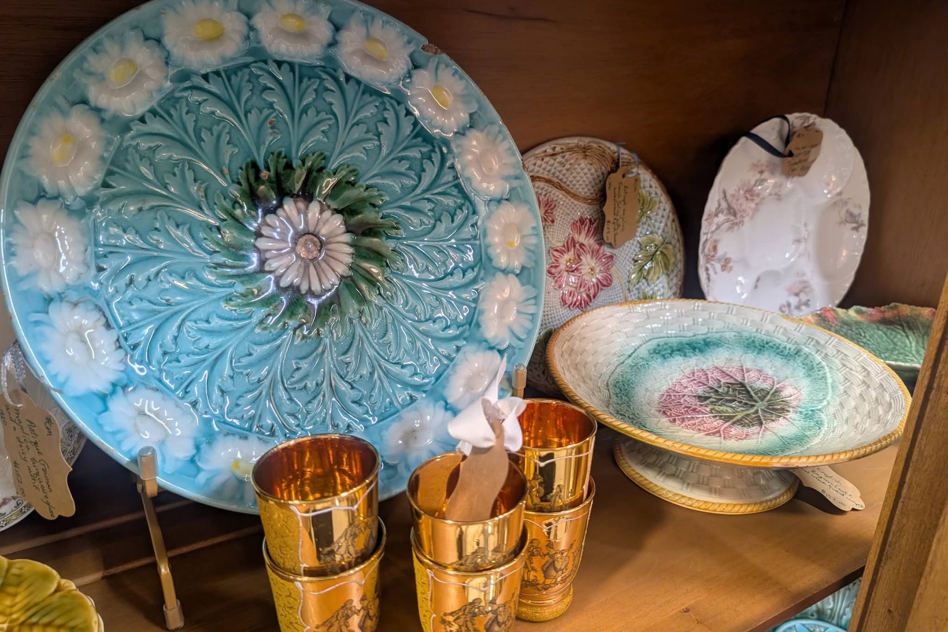 A shelf displays a sunflower planter with yellow flowers, two amber glasses, and two lit candles on blue stands. Several lampshades are in the background.
