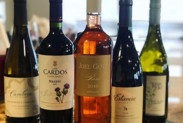 Five bottles of wine are displayed upright in a row on a table, including red, white, and rosé varieties. The center bottle is a 2016 Joel Gott Rosé. The labels of the bottles are clearly visible.