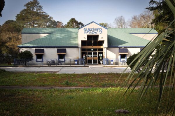 A restaurant named Baxters with a green roof and beige walls, seen from the parking lot, surrounded by trees and greenery on a sunny day.