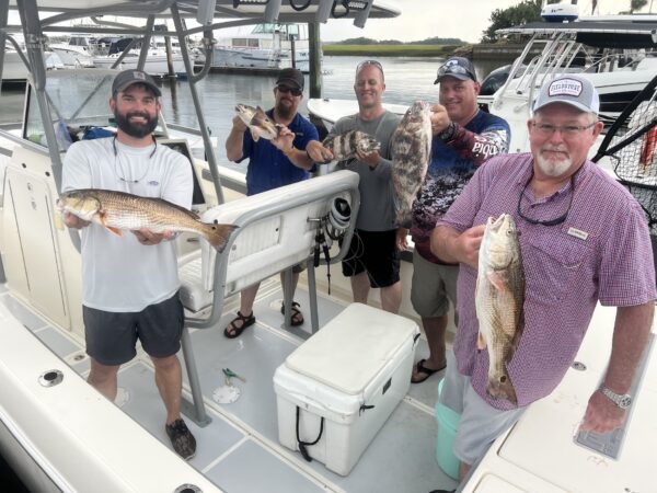 Five men on a boat docked at a marina proudly hold up their freshly caught fish, smiling at the camera. Various fishing equipment and other boats are visible in the background.