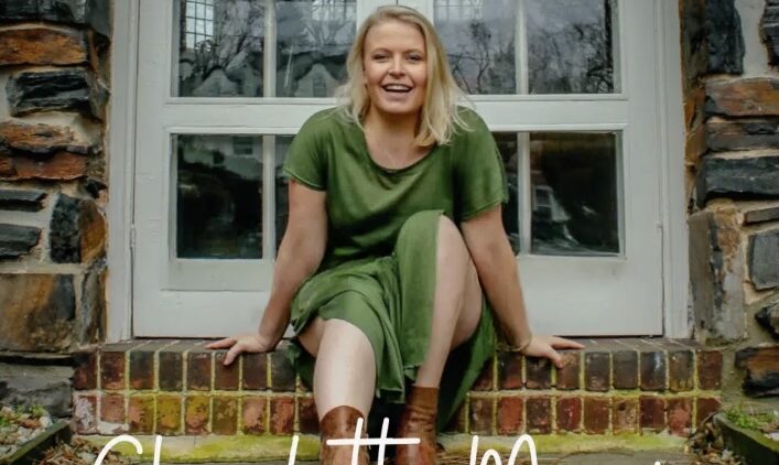 A woman in a green dress and brown boots sits smiling on brick steps in front of a glass door. The name Charlotte Morris is written in white script at the bottom of the image.