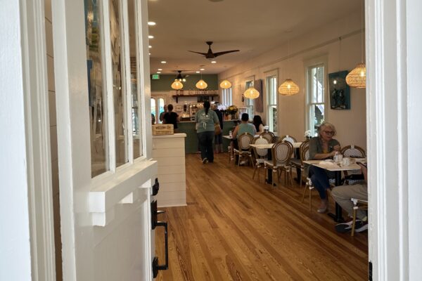 Interior of a bright cafe with wood floors, tables for dining, and staff working behind a service counter.