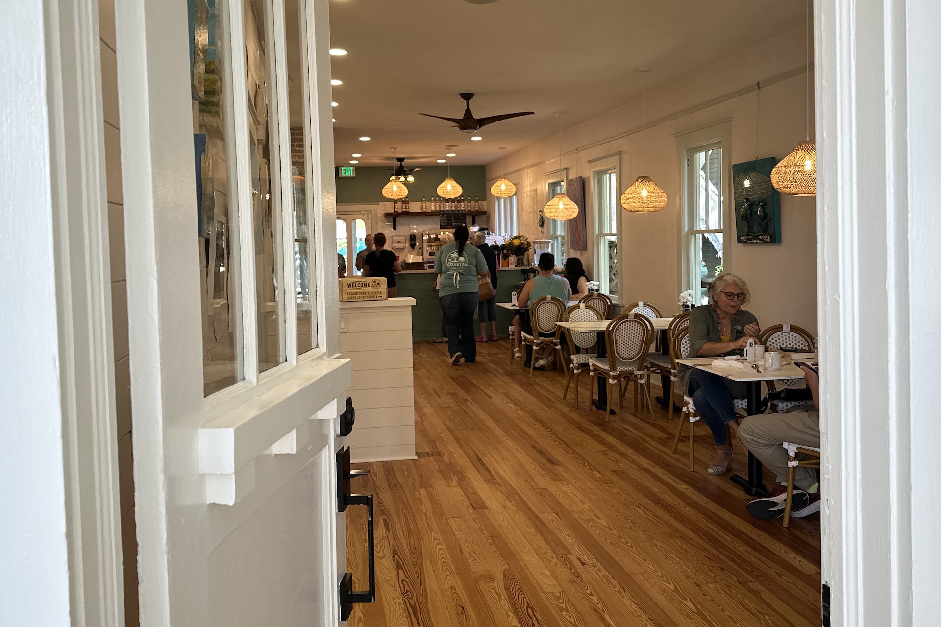 Interior of a bright cafe with wood floors, tables for dining, and staff working behind a service counter.