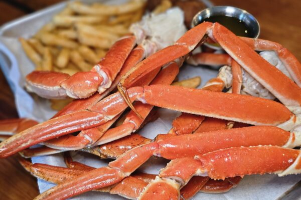 A pile of steamed crab legs served on a metal tray with a side of fries and a small container of melted butter.