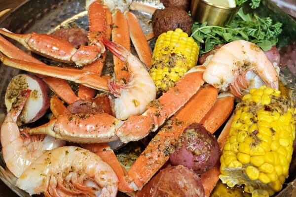 A seafood boil platter with crab legs, shrimp, corn on the cob, red potatoes, sausage, and a hushpuppy.