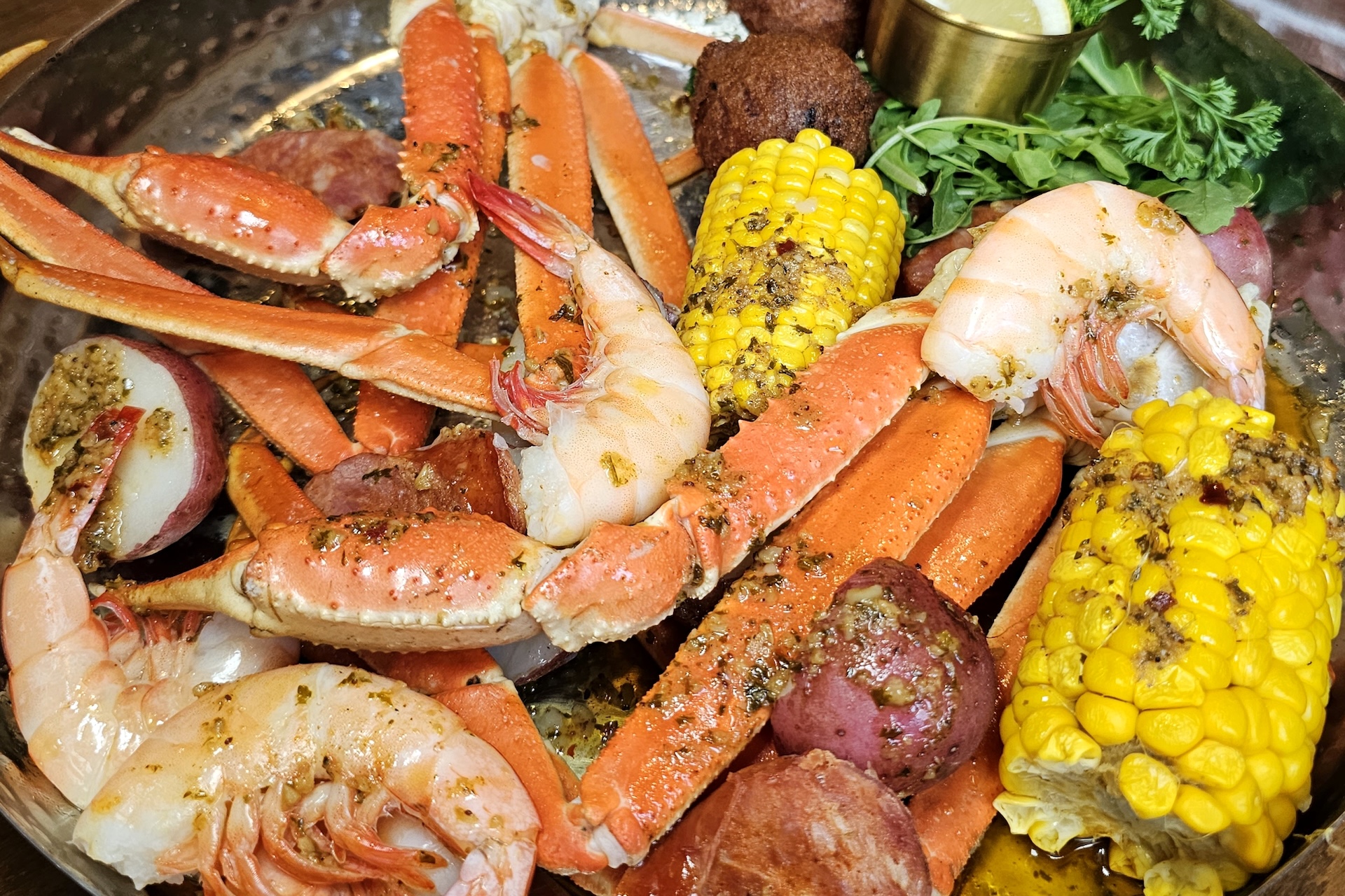 A seafood boil platter with crab legs, shrimp, corn on the cob, red potatoes, sausage, and a hushpuppy.
