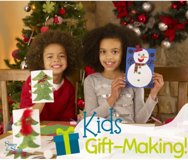 Two smiling children sit at a table holding up handmade holiday cards—a Christmas tree and a snowman—with craft supplies around them. A decorated Christmas tree and fireplace are in the background. Text reads, “Kids Gift-Making!”.