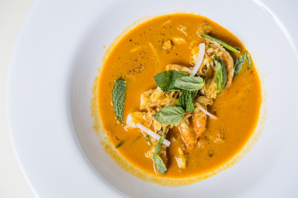 A white plate with shrimp in an orange curry sauce, garnished with fresh mint leaves and herbs.