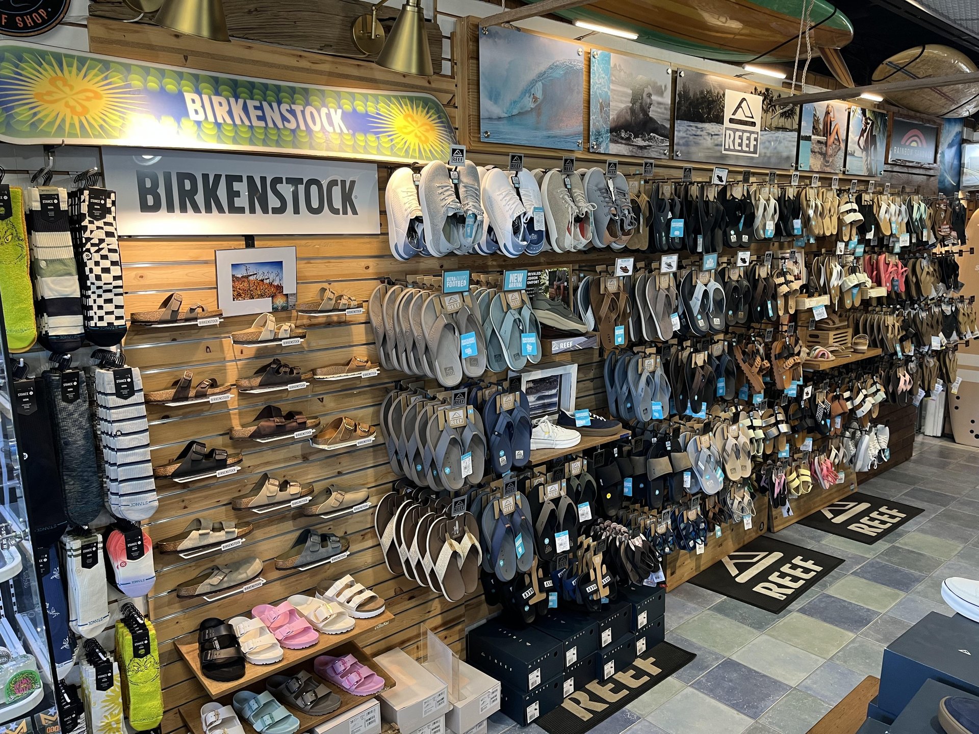 Retail store wall display featuring various Birkenstock and Reef sandals, socks, and branded signage.