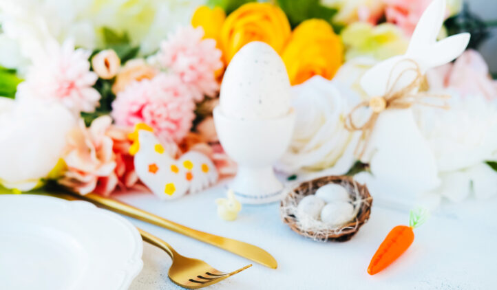 Goldenish fork and knife on white surface with toy cock doodle, quail eggs, Easter bunny and blurred flowers.