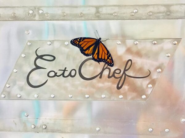 A monarch butterfly rests on a metallic sign that reads EatoChef in cursive script, attached to a riveted metal surface.