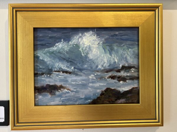 A framed painting depicts ocean waves crashing against dark rocks, with splashes of white foam and shades of blue and green. The frame is gold with a metallic sheen.