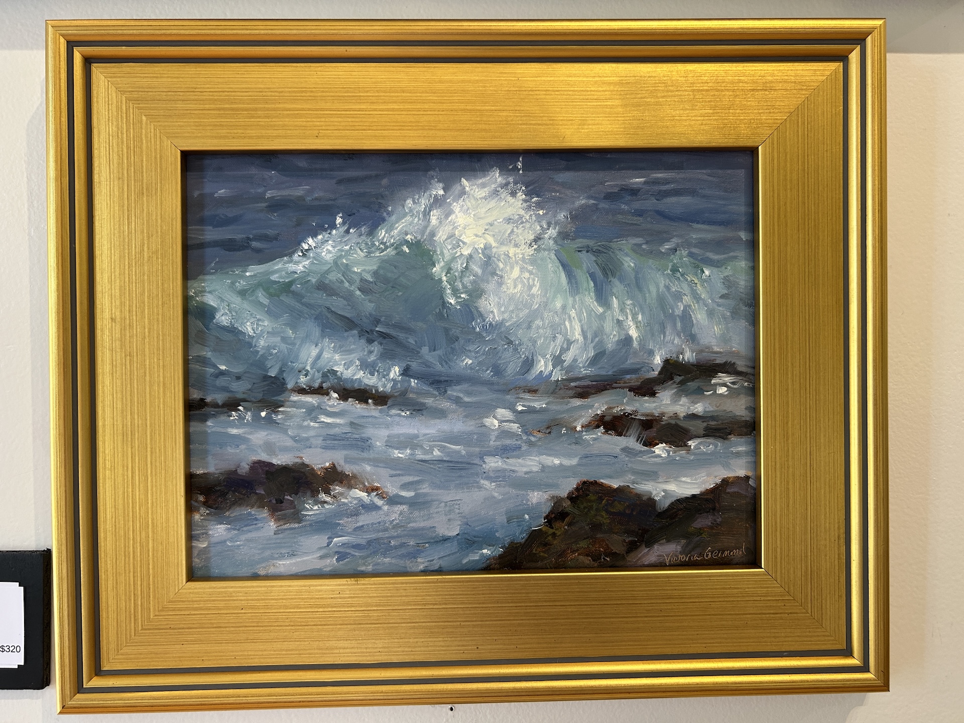 A framed painting depicts ocean waves crashing against dark rocks, with splashes of white foam and shades of blue and green. The frame is gold with a metallic sheen.