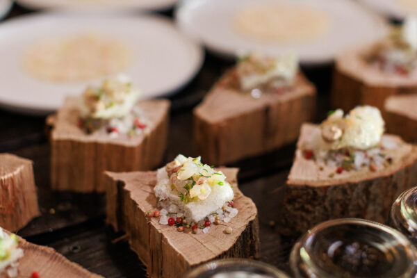 Several appetizers are served on rustic wooden blocks, garnished with herbs and nuts, sitting atop coarse salt and peppercorns. White plates and glass jars are visible in the background.