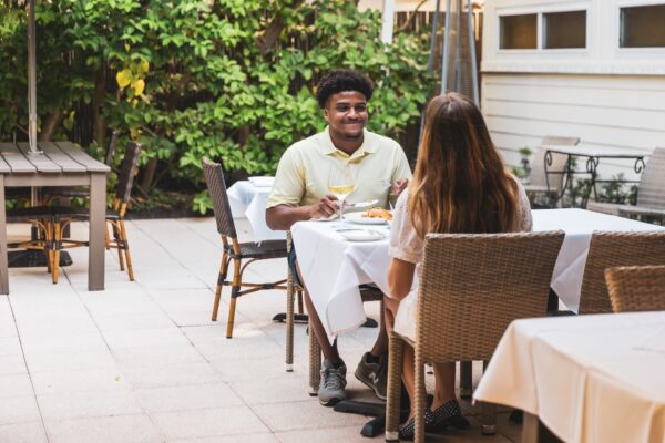A couple dining outdoors at Indigo restaurant on Amelia Island, Florida, seated at a white table with greenery in the background.