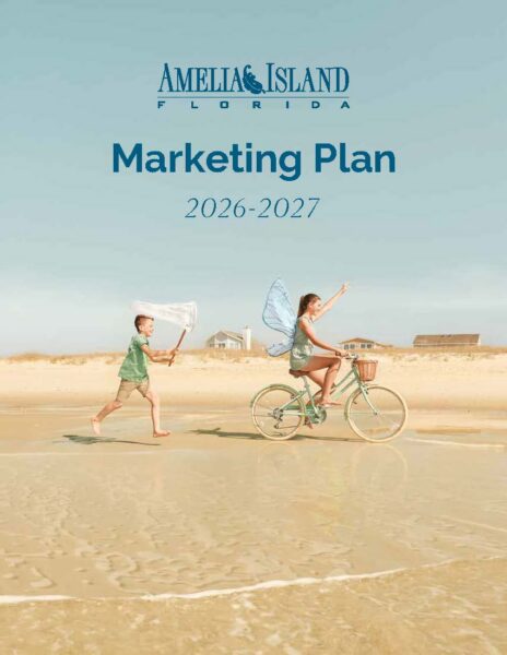 A boy with a net chases a girl in fairy wings riding a bike on a sandy beach under a blue sky. Text reads: Amelia Island Florida Marketing Plan 2026-2027..