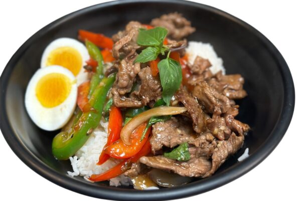 A black bowl filled with white rice, stir-fried beef, sliced red and green peppers, onions, fresh basil, and two halves of a boiled egg.