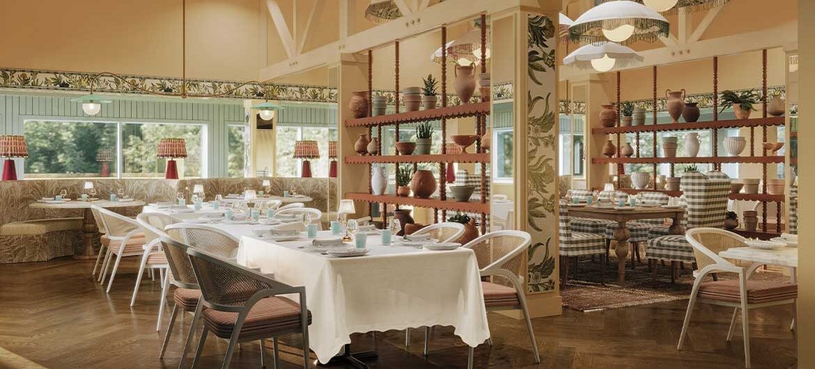 A bright, elegant restaurant interior with white tablecloths, checkered cushioned chairs, wooden floors, decorative shelving with plants and vases, and large windows letting in natural light.