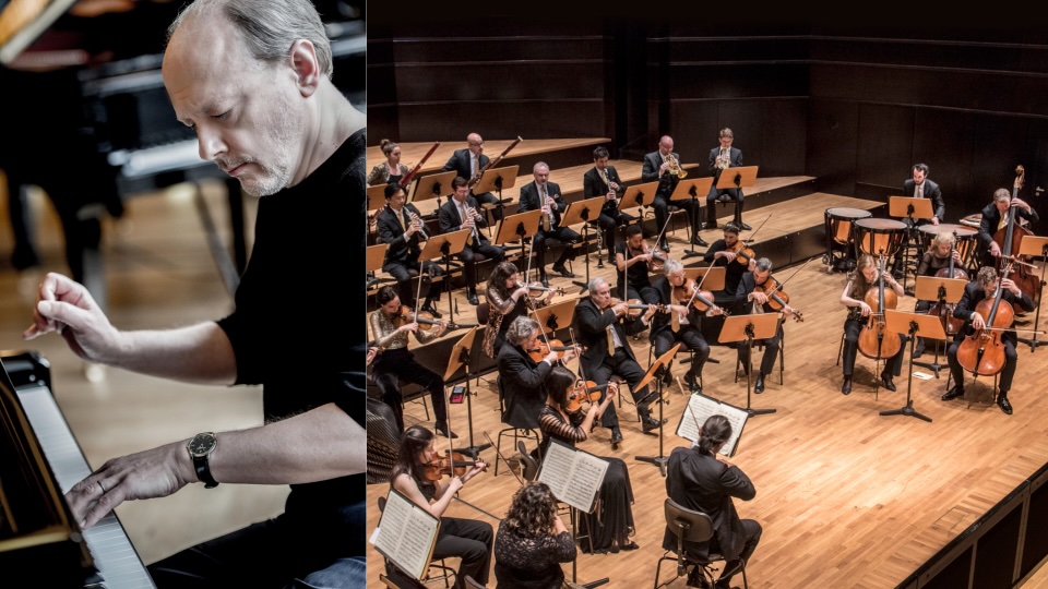 A man plays a grand piano on the left, while an orchestra with string and wind instruments performs on stage on the right. The musicians are seated in a concert hall with wooden floors.