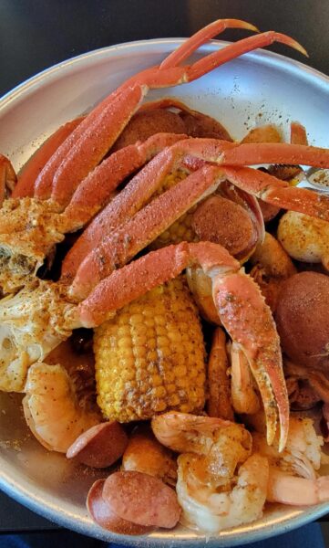 A bowl filled with crab legs, shrimp, sausage slices, corn on the cob, and potatoes, all seasoned with spices.