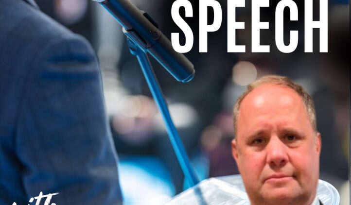 A close-up of a microphone on a stand with the text The Power of Speech with Steve Skolnick. A man in a suit appears in the bottom right corner. The background is blurred, showing an indoor event setting.