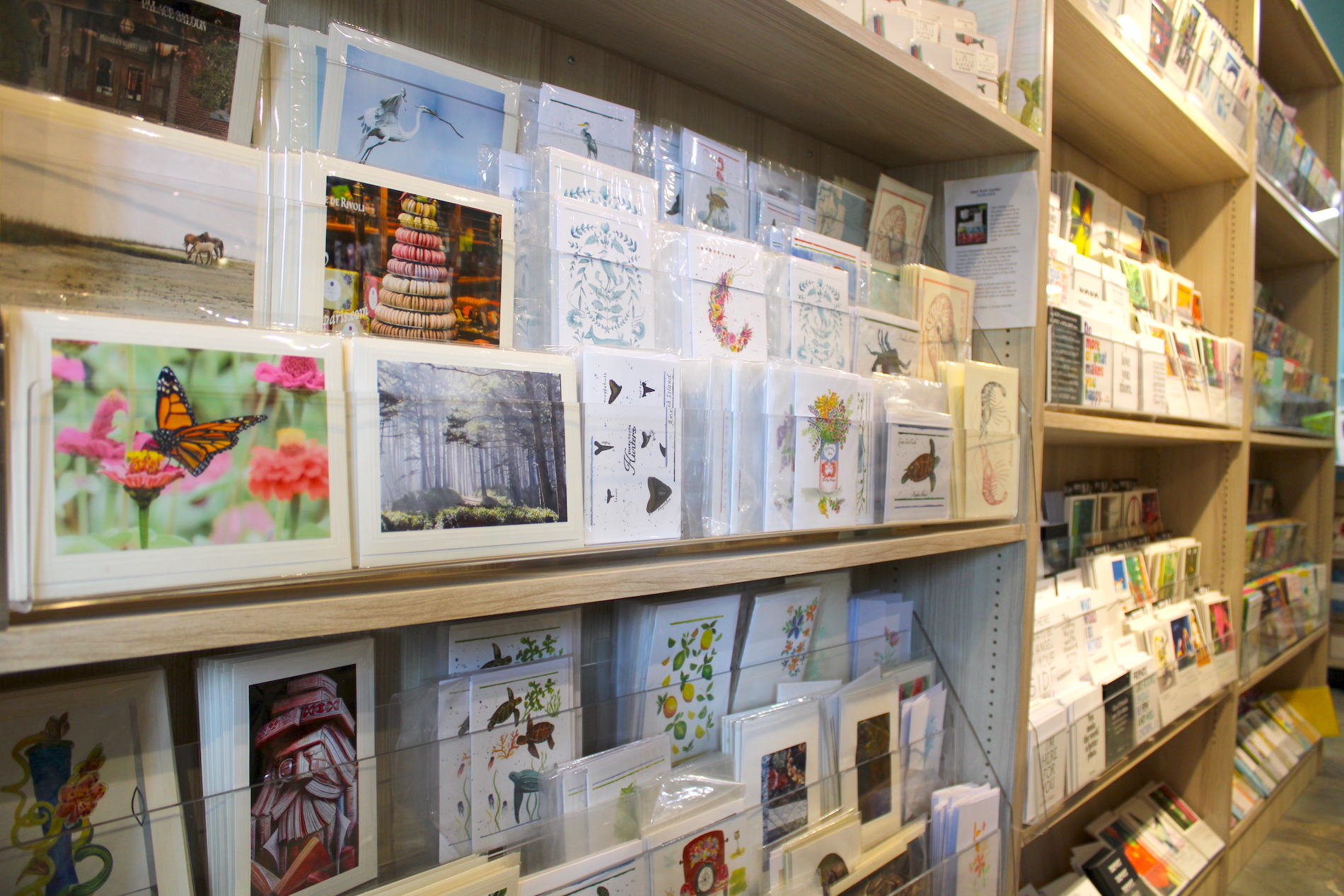Shelves filled with colorful greeting cards and postcards featuring various designs, such as animals, nature scenes, and artistic illustrations, displayed in a well-lit store.