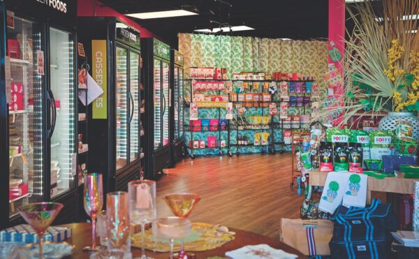 A brightly lit pet store interior featuring refrigerators with frozen foods on the left, shelves stocked with colorful pet supplies at the back, and displays with toys, treats, and glasswares on the right.