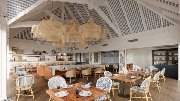 Coastal-style restaurant with high, beamed ceiling, wicker chandeliers, patterned blue and white chairs, wooden tables set with napkins and glasses, and a bright, airy ambiance.