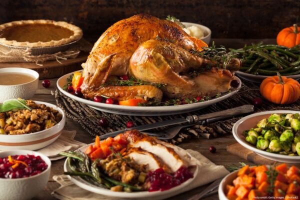 A festive table set with a roasted turkey, stuffing, green beans, sweet potatoes, Brussels sprouts, cranberry sauce, gravy, pumpkin pie, and small pumpkins, arranged for a Thanksgiving meal.