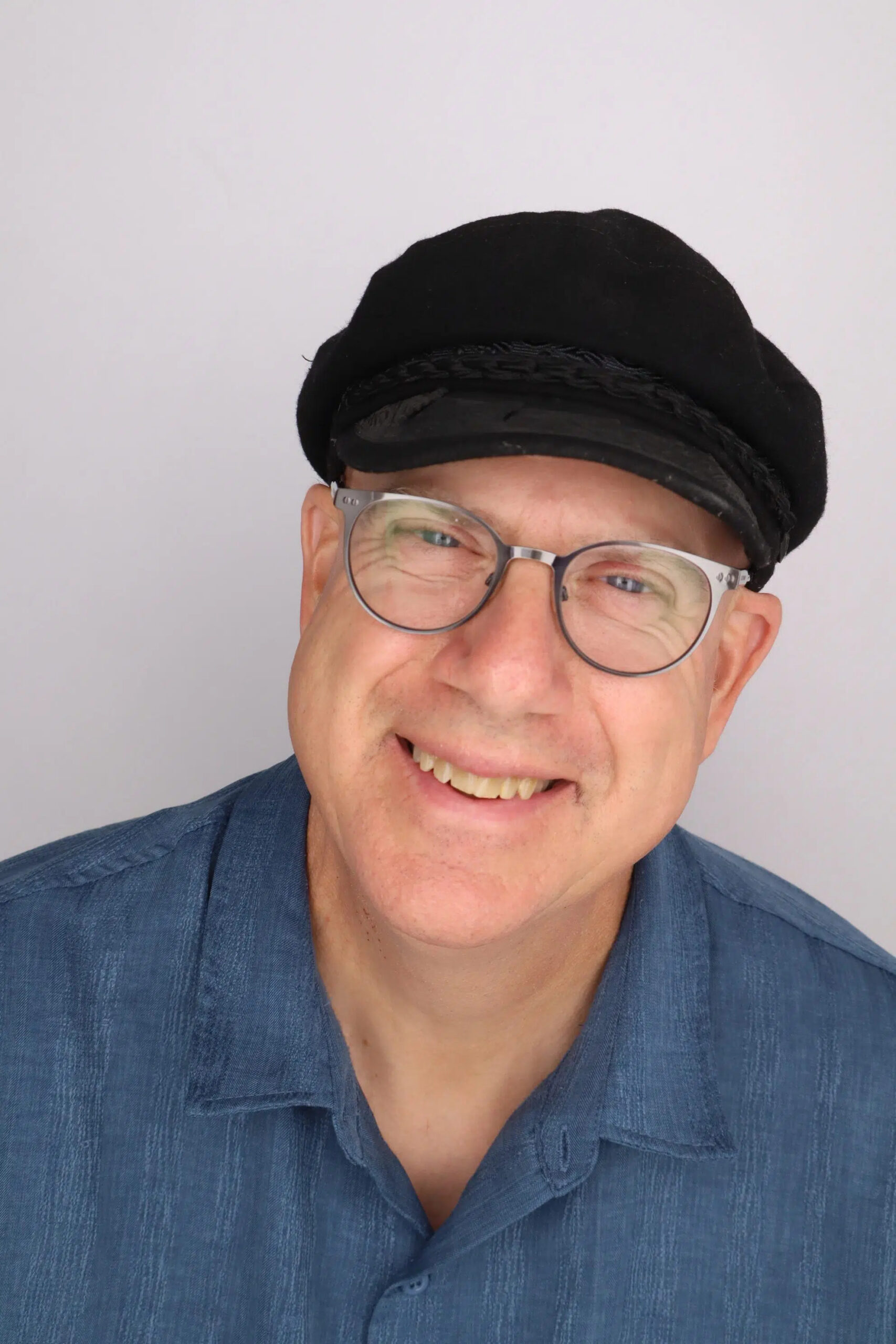A smiling middle-aged man wearing glasses and a black peaked cap.