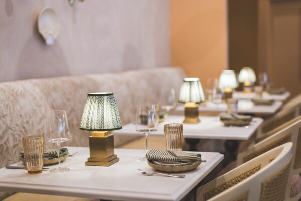 Elegant restaurant table setting with gold and green lamps, striped napkins, glassware, and neutral-colored chairs, creating a cozy and inviting dining atmosphere.