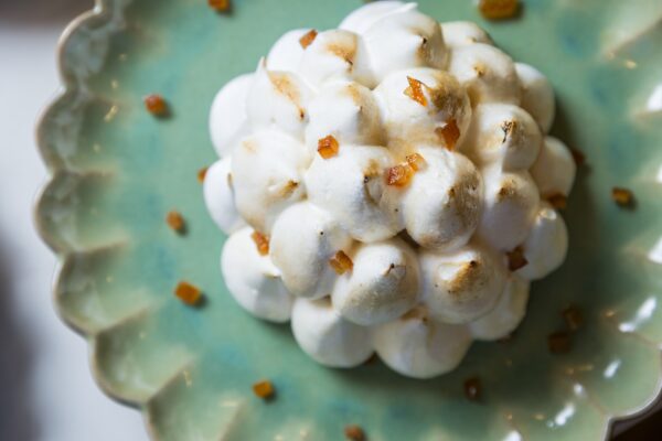 A close-up of a dessert topped with toasted meringue dollops and small pieces of candied fruit, served on a green, scalloped-edged plate.