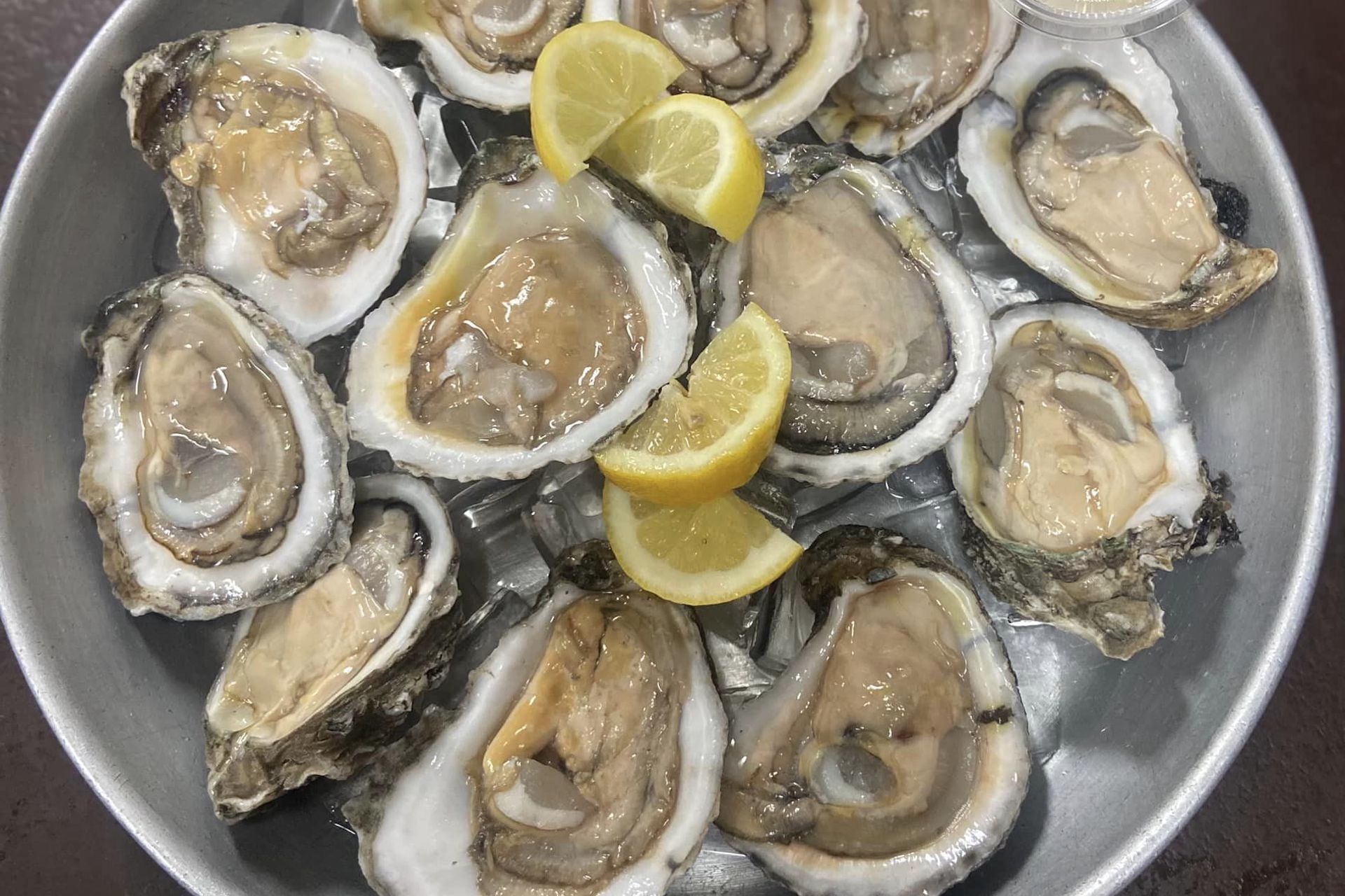 A metal plate filled with raw oysters on the half shell, served on ice with lemon wedges in the center.